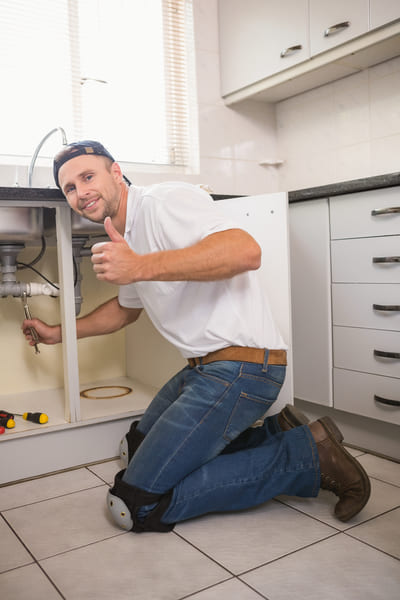 A man giving a thumbs up while working on a kitchen sink.