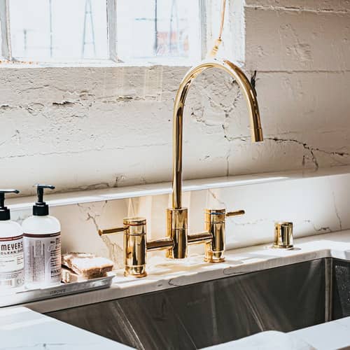 A kitchen sink with a brass faucet and soap dispenser.
