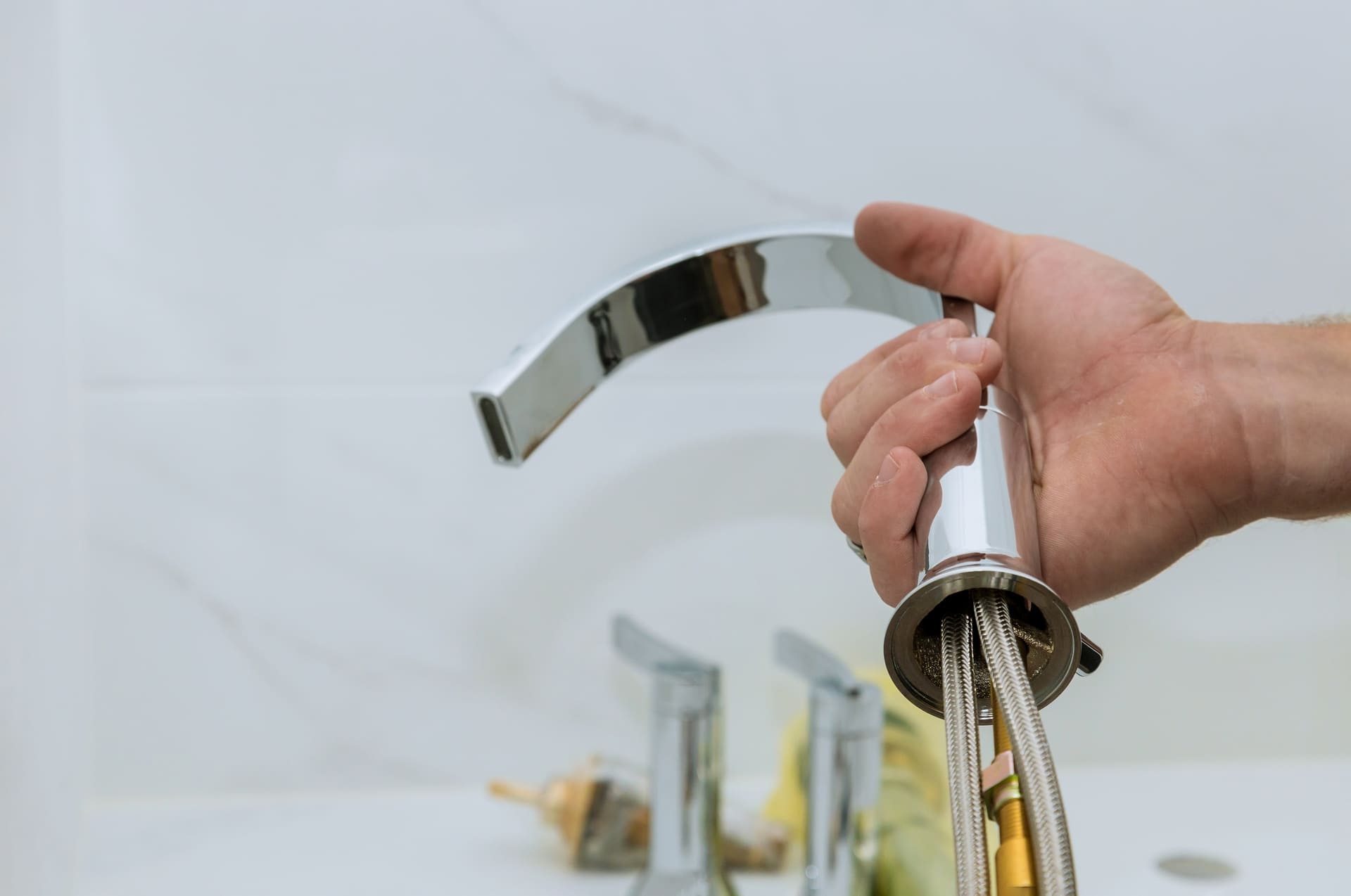 A person is holding a faucet in front of a sink.